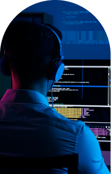 Homem jovem, branco, cabelo curto, usando uma camisa branca, de costas para nós, programando em seu computador